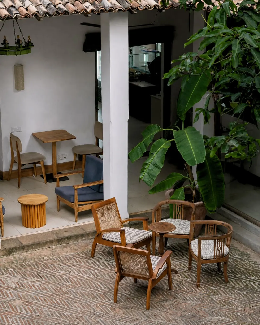 A cluster of rattan and timber chairs on brick laid in a zigzag beside a banana plant in the courtyard.