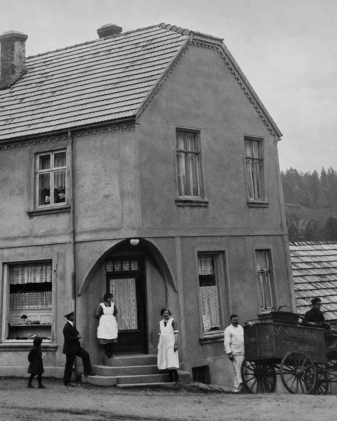 Black-and-white photograph of people outside a building, with a cart beside the entrance.